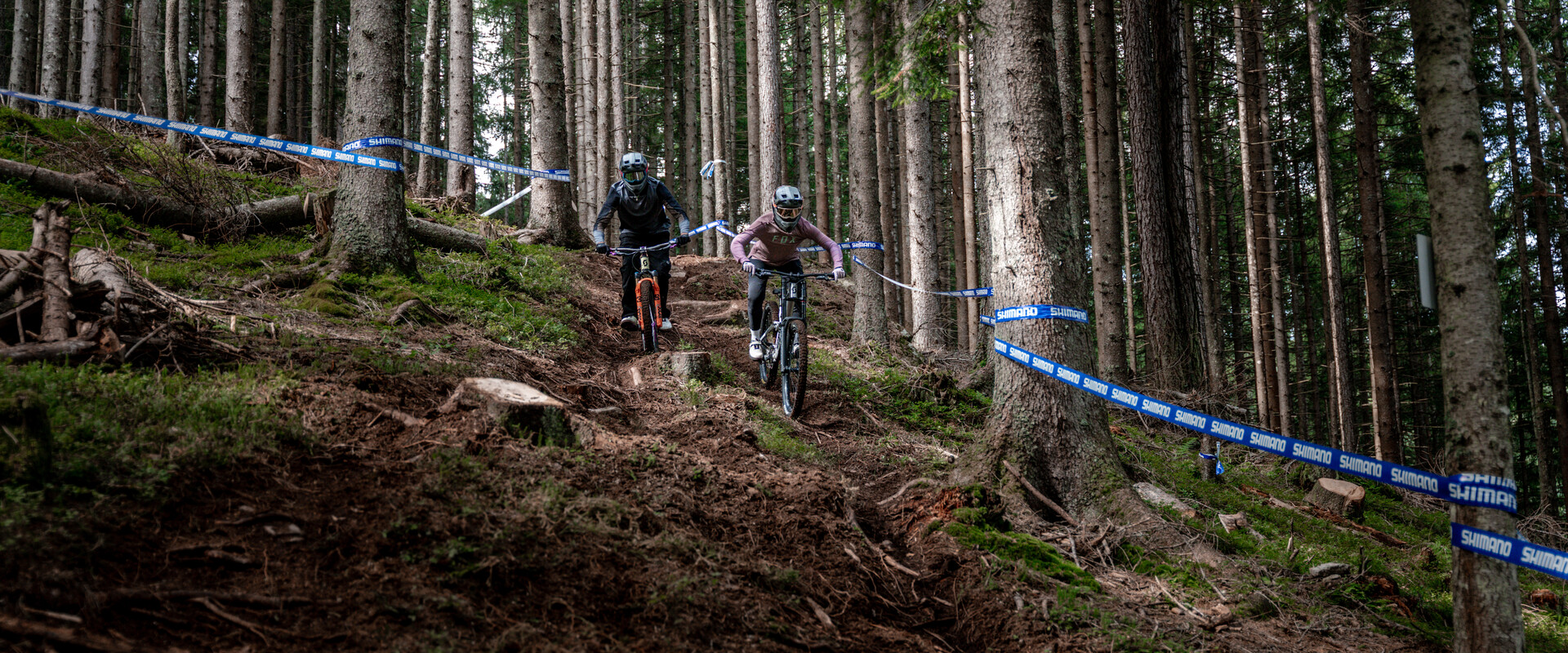 Zwei Mountainbiker:innen fahren mit vollem Fokus ein steiles, wurzeliges Waldstück entlang.  | © Yvonne Hörl
