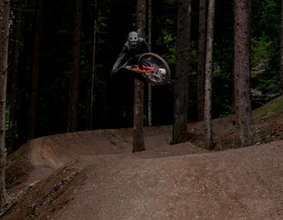 Ein Rider hebt auf der T-Line im Wald ab und schwebt mit seinem Bike elegant über einen Kicker – ein klassischer Style-Move auf dem Flow-Trail. | © Yvonne Hörl
