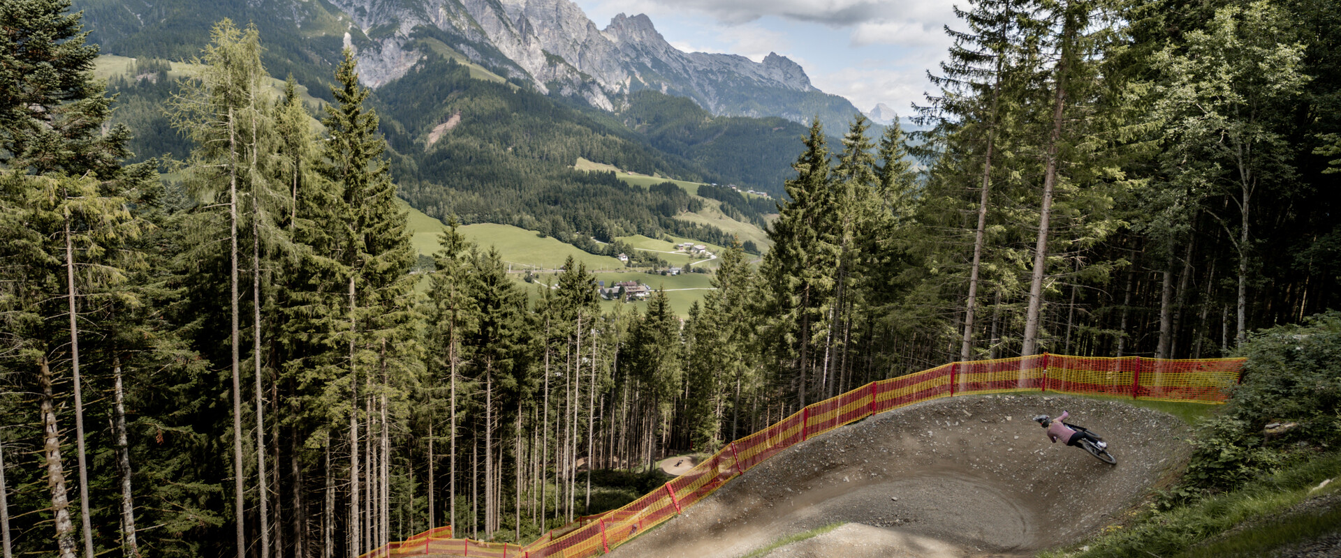 Mountainbiker in einem großen Anlieger der T-Line, die sich durch den Wald schlängelt. Im Hintergrund das beeindruckende Panorama der Leoganger Steinberge. | © Yvonne Hörl
