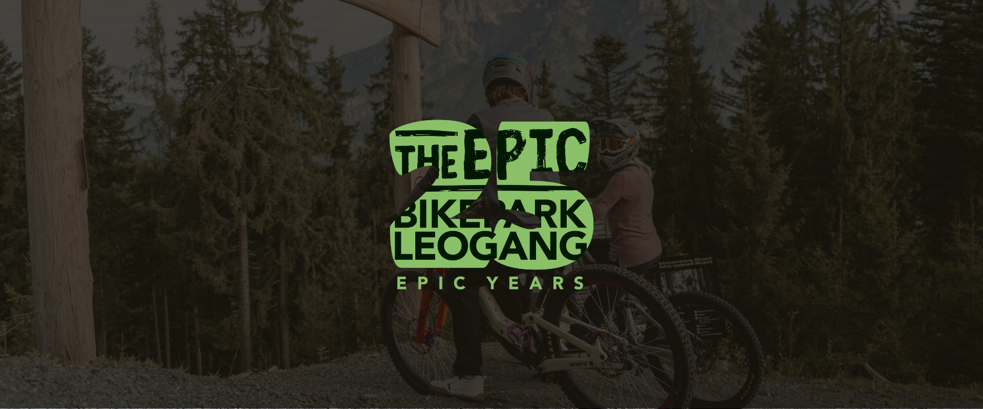 Zwei Mountainbiker am Einstieg des Epic Bikepark Leogang mit Logo „Epic Years“ vor alpiner Waldkulisse. | © Yvonne Hörl