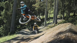 Mountainbiker springt über einen Jump auf einem Flowtrail im EPIC Bikepark Leogang, während weitere Rider:innen der Strecken folgen. | © Moritz Ablinger