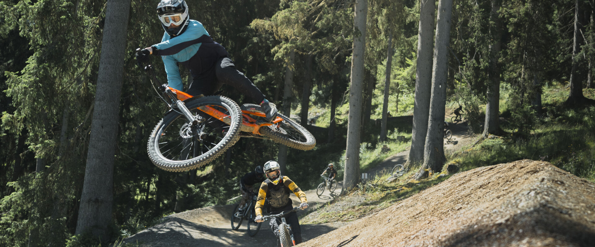 Mountainbiker springt über einen Jump auf einem Flowtrail im EPIC Bikepark Leogang, während weitere Rider:innen der Strecken folgen. | © Moritz Ablinger